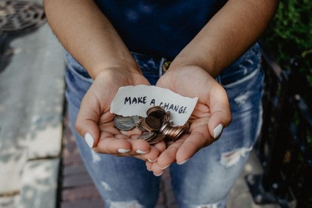 Vrouw die munten en een briefje met make a change vasthoudt.
